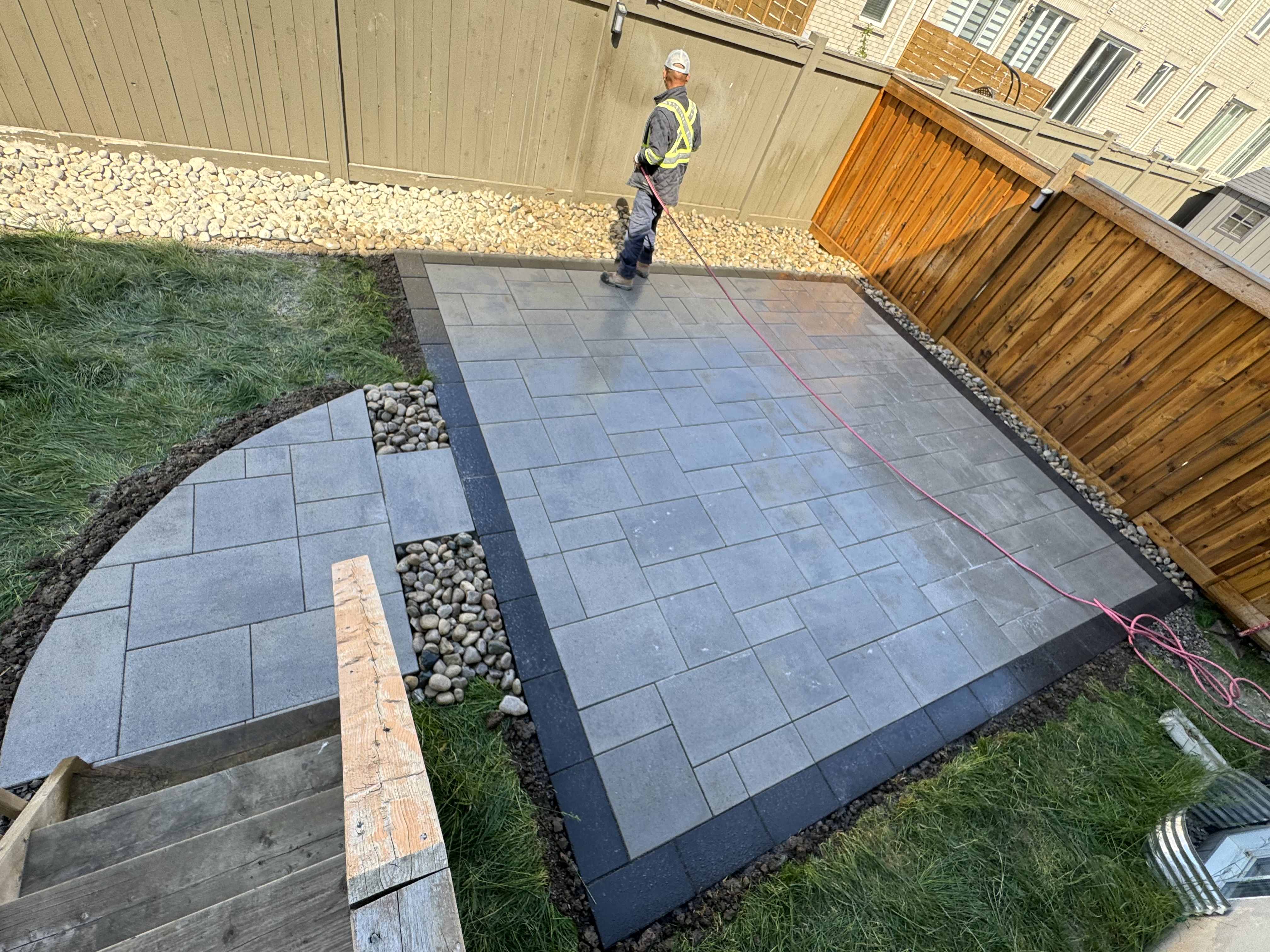 Completed backyard interlock patio with curved pathway and river rock