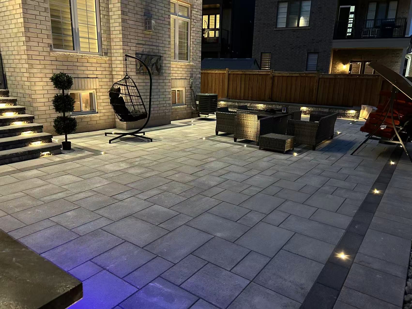 Completed backyard interlock patio at night with ground lighting
